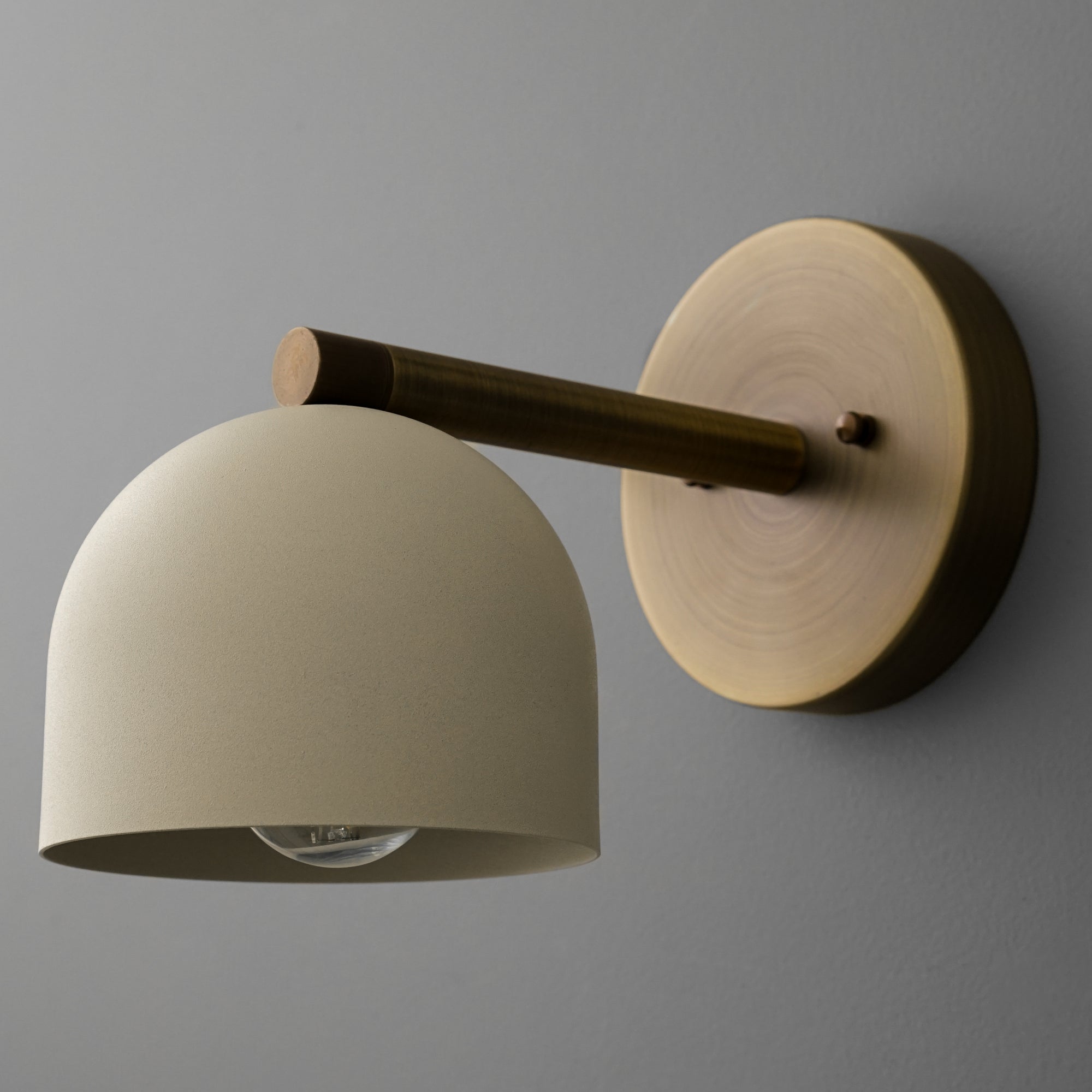 Antique brass wall sconce with cream dome shade and exposed bulb on gray wall. - Sconce Model No. 5356
