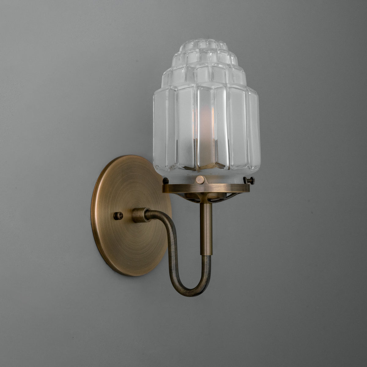 Wall-mounted brass sconce with a curved arm and ribbed clear glass shade housing one bulb. - SCONCE MODEL NO. 1035