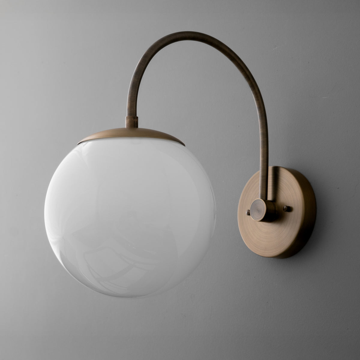 Wall sconce with antique brass finish and white frosted glass globe shade on curved arm against gray background. - SCONCE MODEL NO. 2947