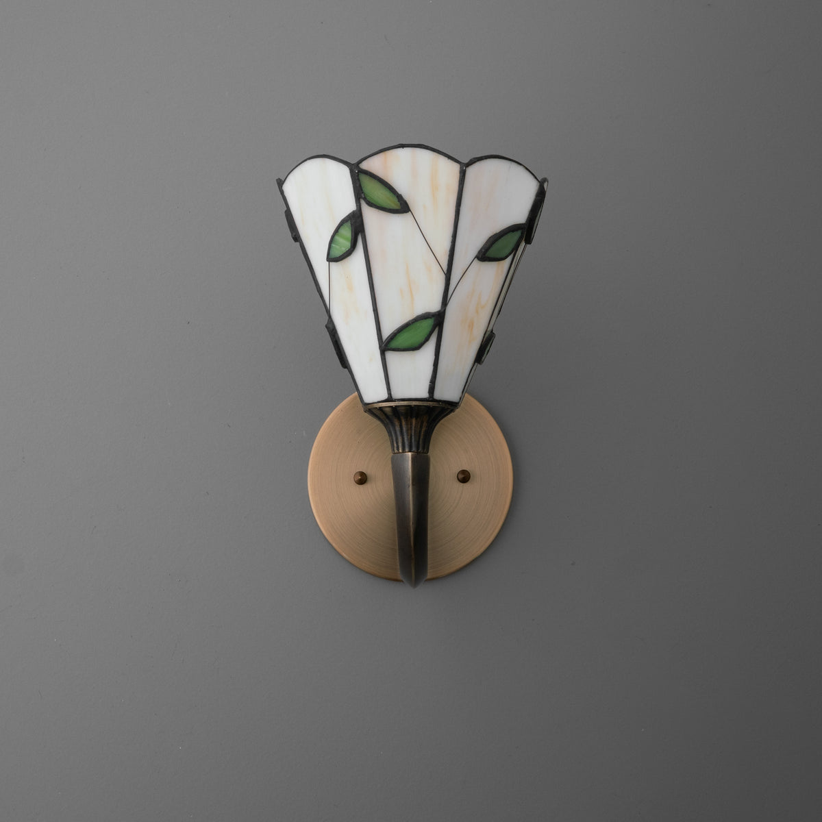Wall sconce with stained glass shade featuring white panels and green leaf accents, mounted on bronze circular base. - SCONCE MODEL NO. 1056