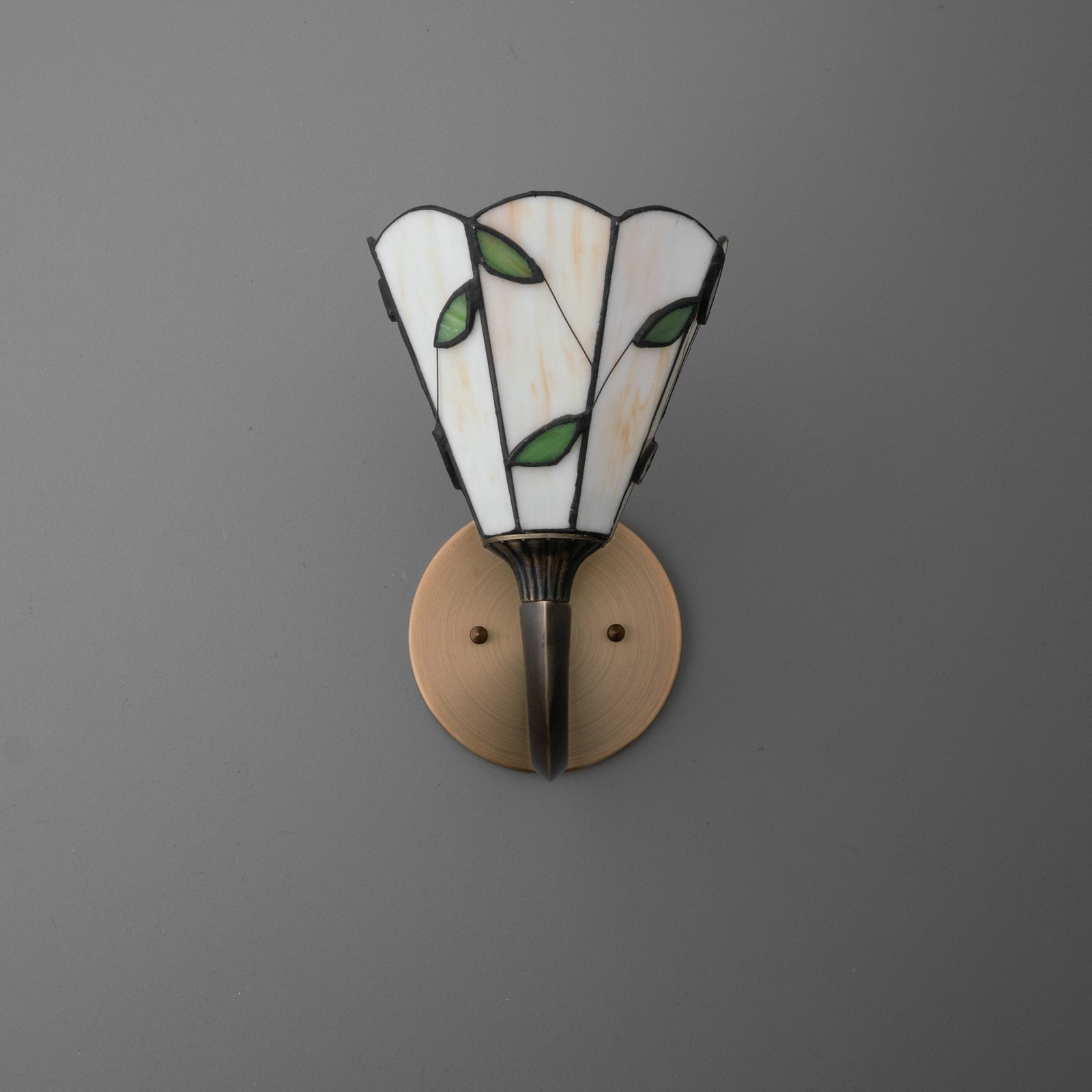 Wall sconce with stained glass shade featuring white panels and green leaf accents, mounted on bronze circular base. - SCONCE MODEL NO. 1056