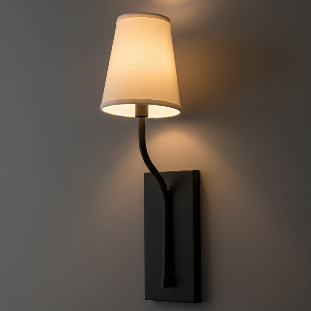 Black metal wall sconce with curved arm and white fabric tapered shade illuminating warm light. - SCONCE MODEL NO. 9714