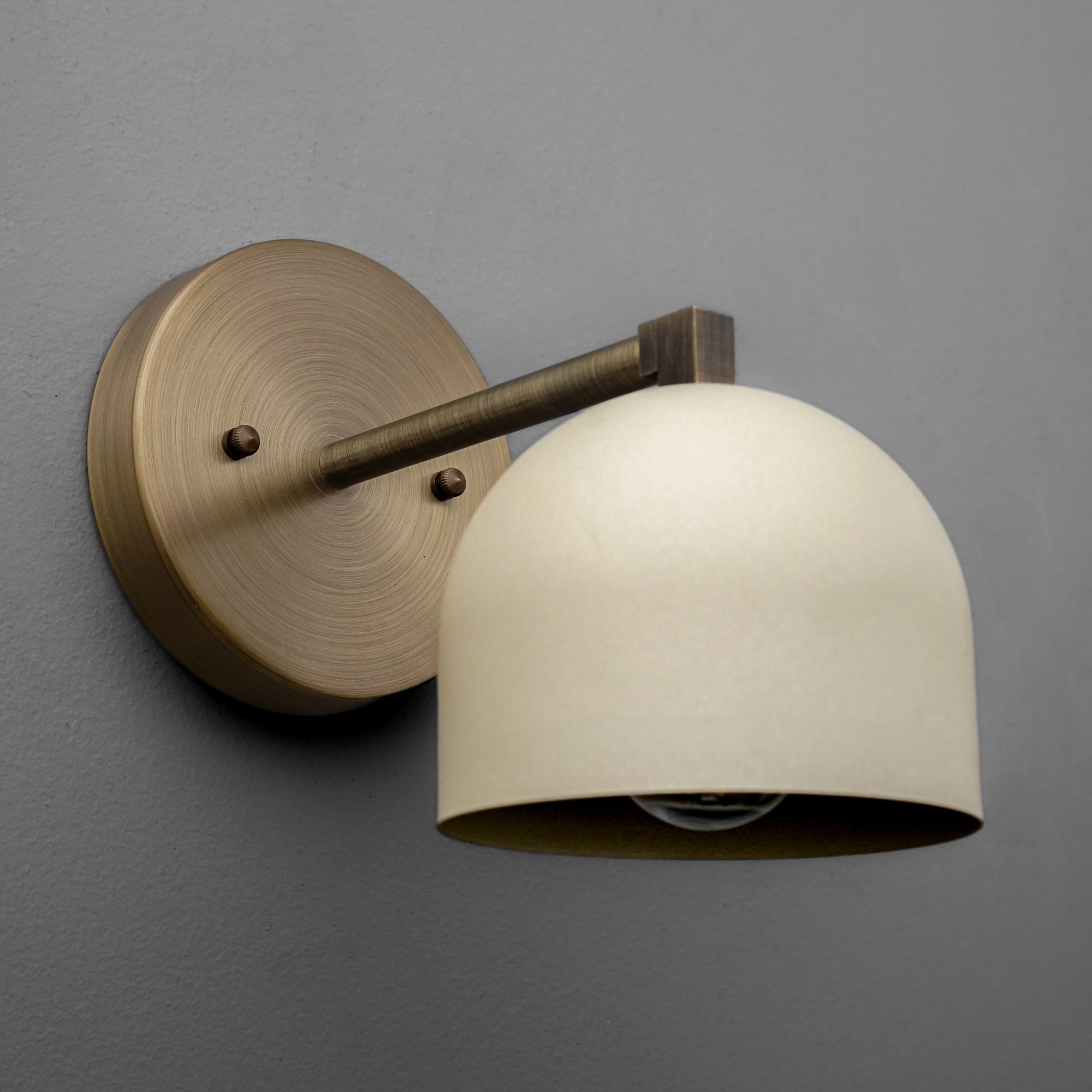 Antique brass wall sconce with cream domed glass shade and round backplate on gray wall. - SCONCE MODEL NO. 3622