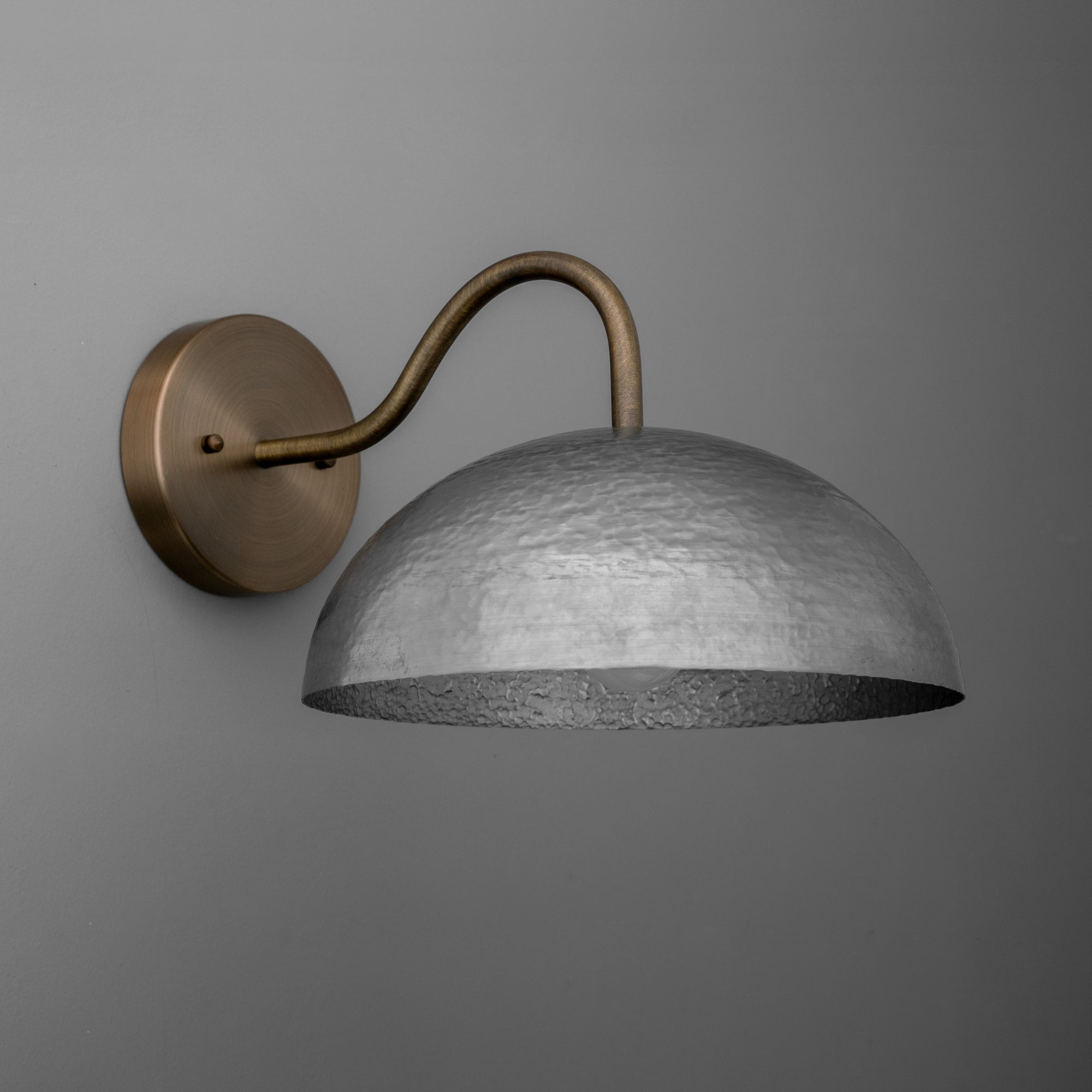 Wall sconce with matte brass curved arm and textured aged steel dome shade on dark gray wall. - SCONCE MODEL NO. 9874