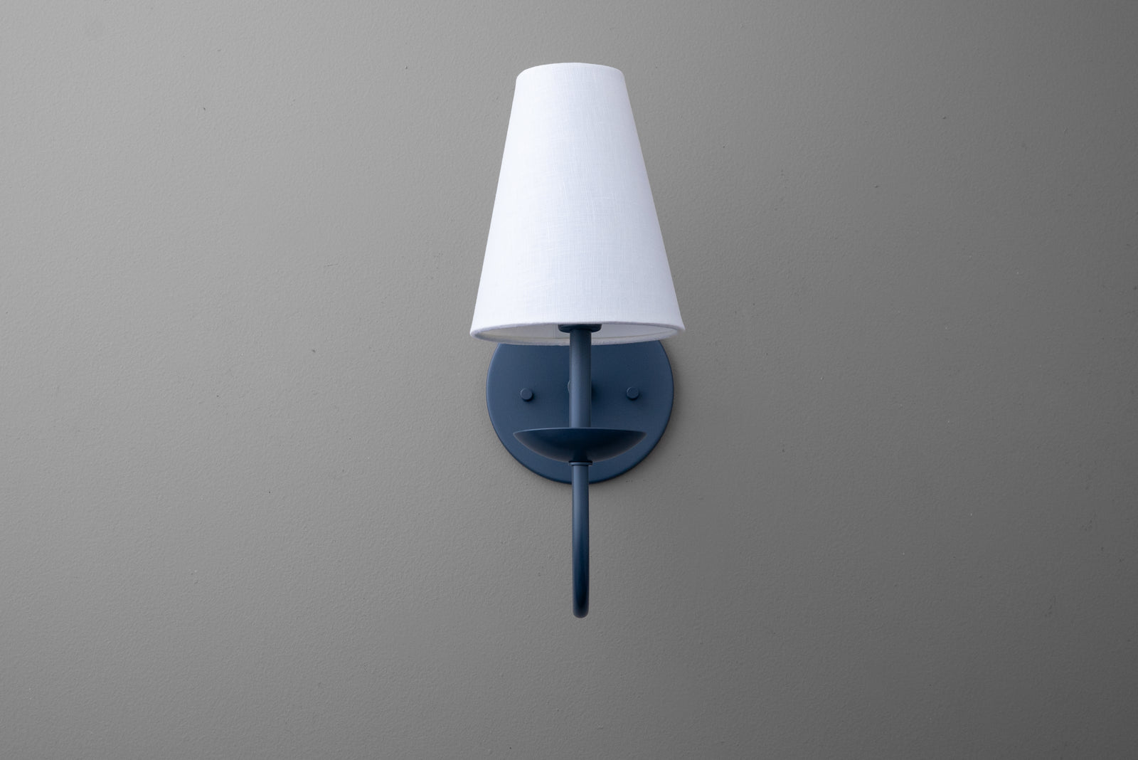 Wall-mounted black metal sconce with a white tapered fabric lampshade against a gray wall. - SCONCE MODEL NO. 7085