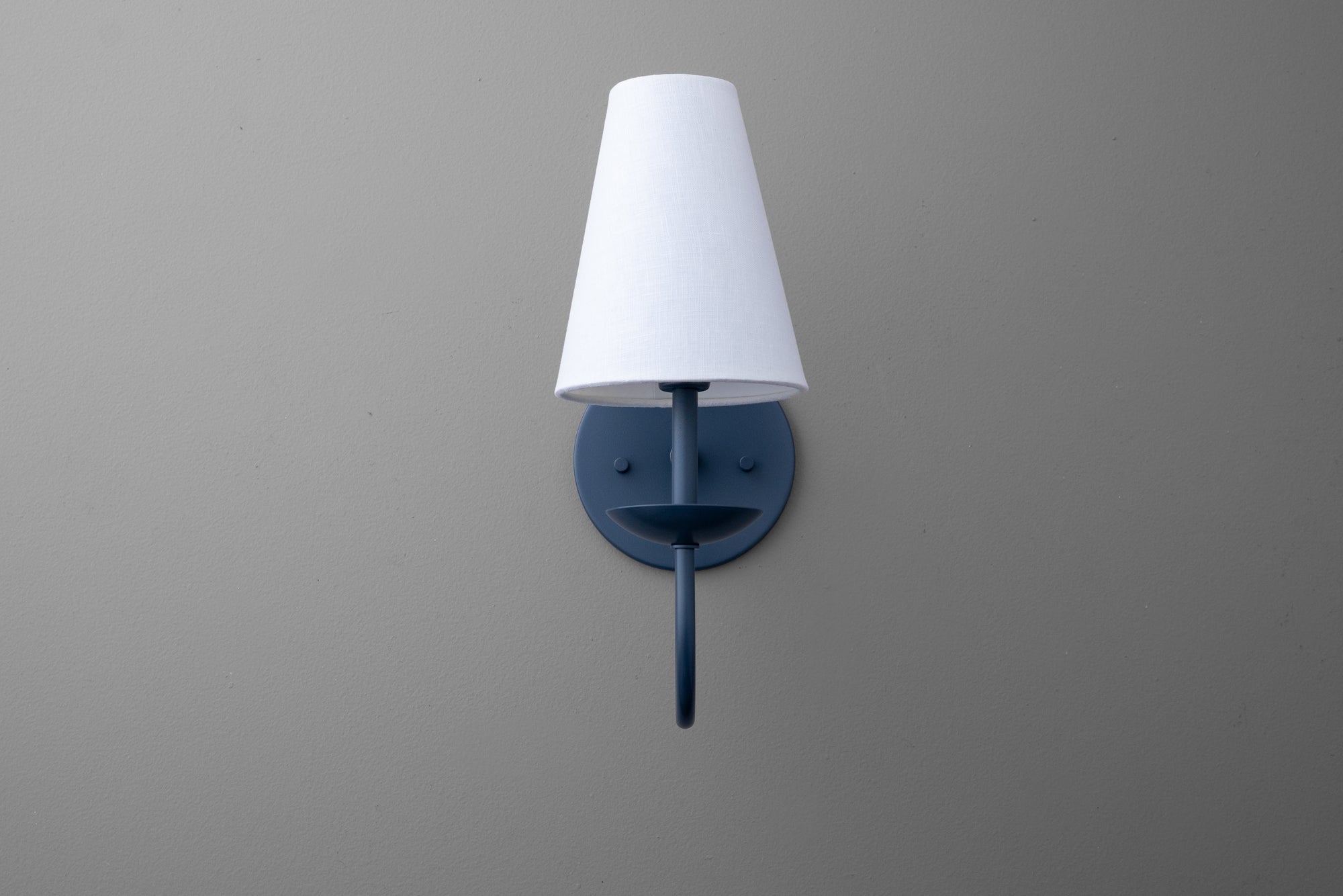 Wall-mounted black metal sconce with a white tapered fabric lampshade against a gray wall. - SCONCE MODEL NO. 7085
