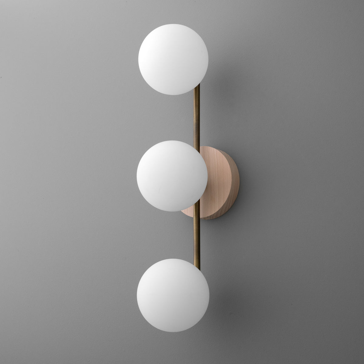 Modern vertical wall sconce with three white frosted glass globes and brushed brass rod on round wood base. - SCONCE MODEL NO. 6089