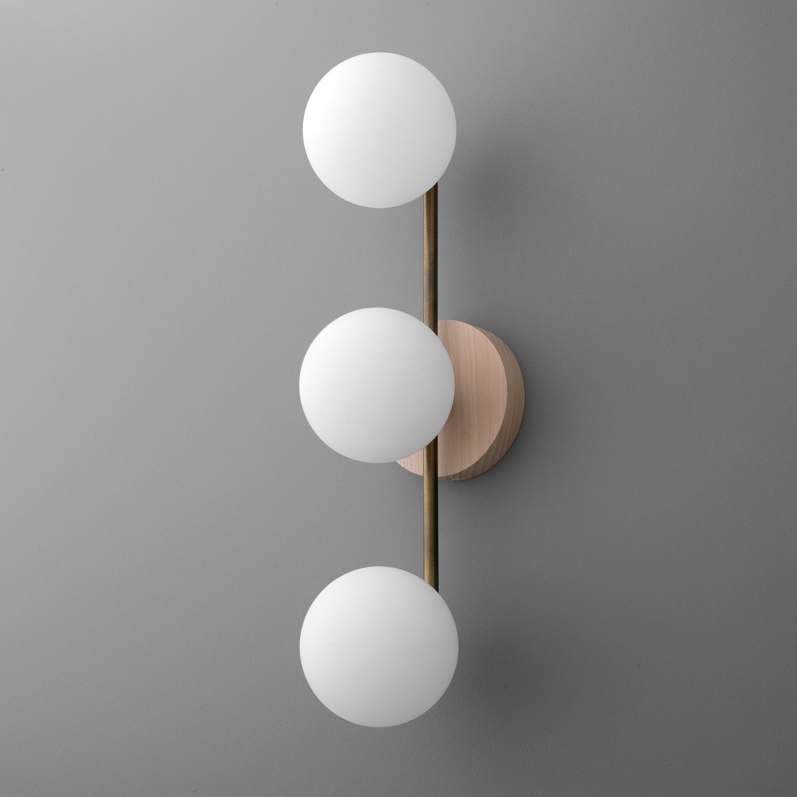 Modern vertical wall sconce with three white frosted glass globes and brushed brass rod on round wood base. - SCONCE MODEL NO. 6089