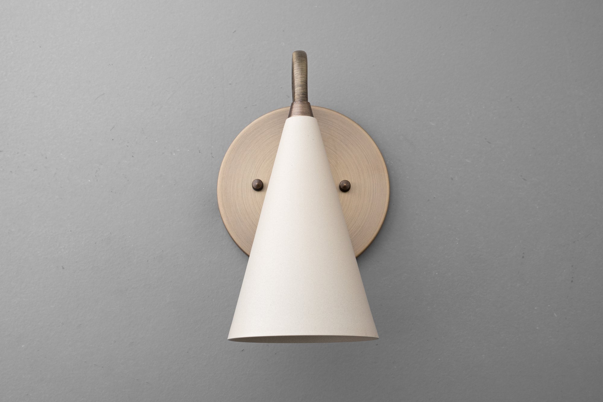 Wall sconce with antique brass finish and cream conical shade mounted on gray wall. - Sconce Model No. 2900