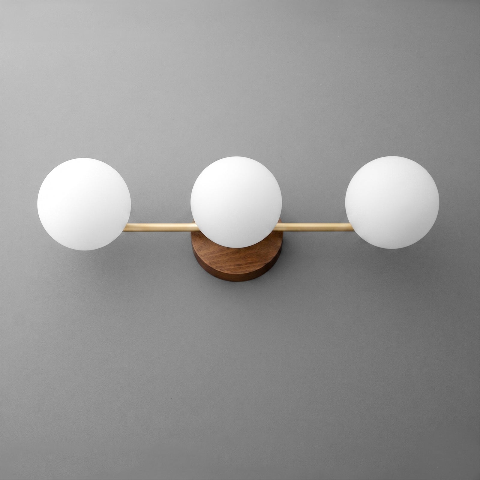 Wall-mounted vanity light with three round white glass globes and a brass horizontal bar over a circular wood base. - VANITY LIGHT MODEL NO. 6089