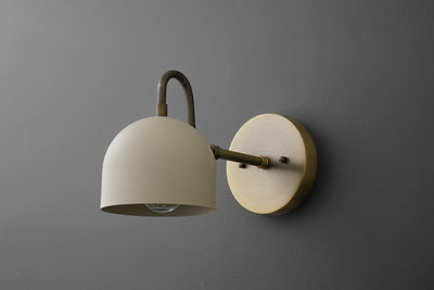 Antique brass wall sconce with cream dome shade and round backplate on gray wall. - SCONCE MODEL NO. 3628