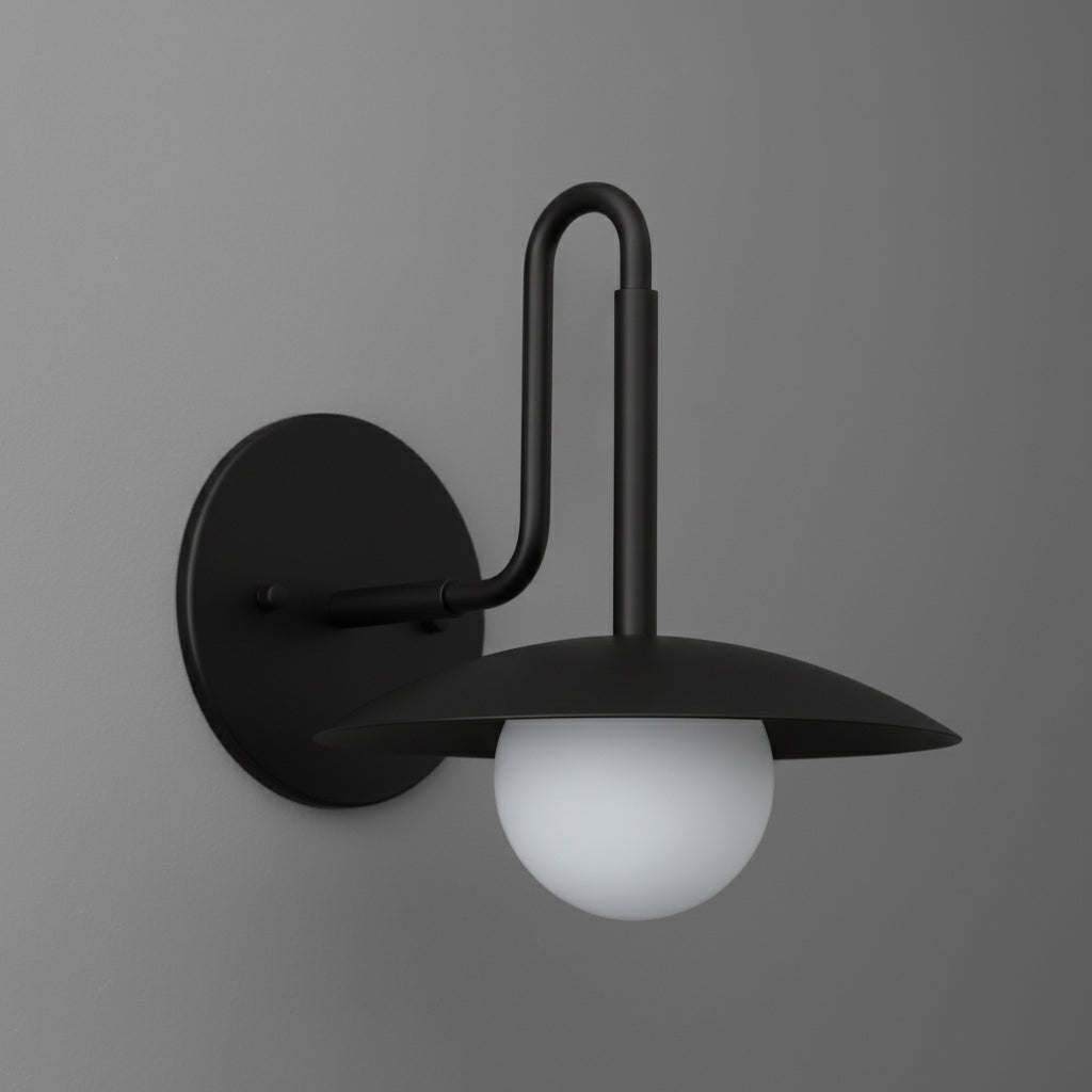 Matte black metal wall sconce with curved arm and flat round shade above white glass globe bulb. - SCONCE MODEL NO. 1013