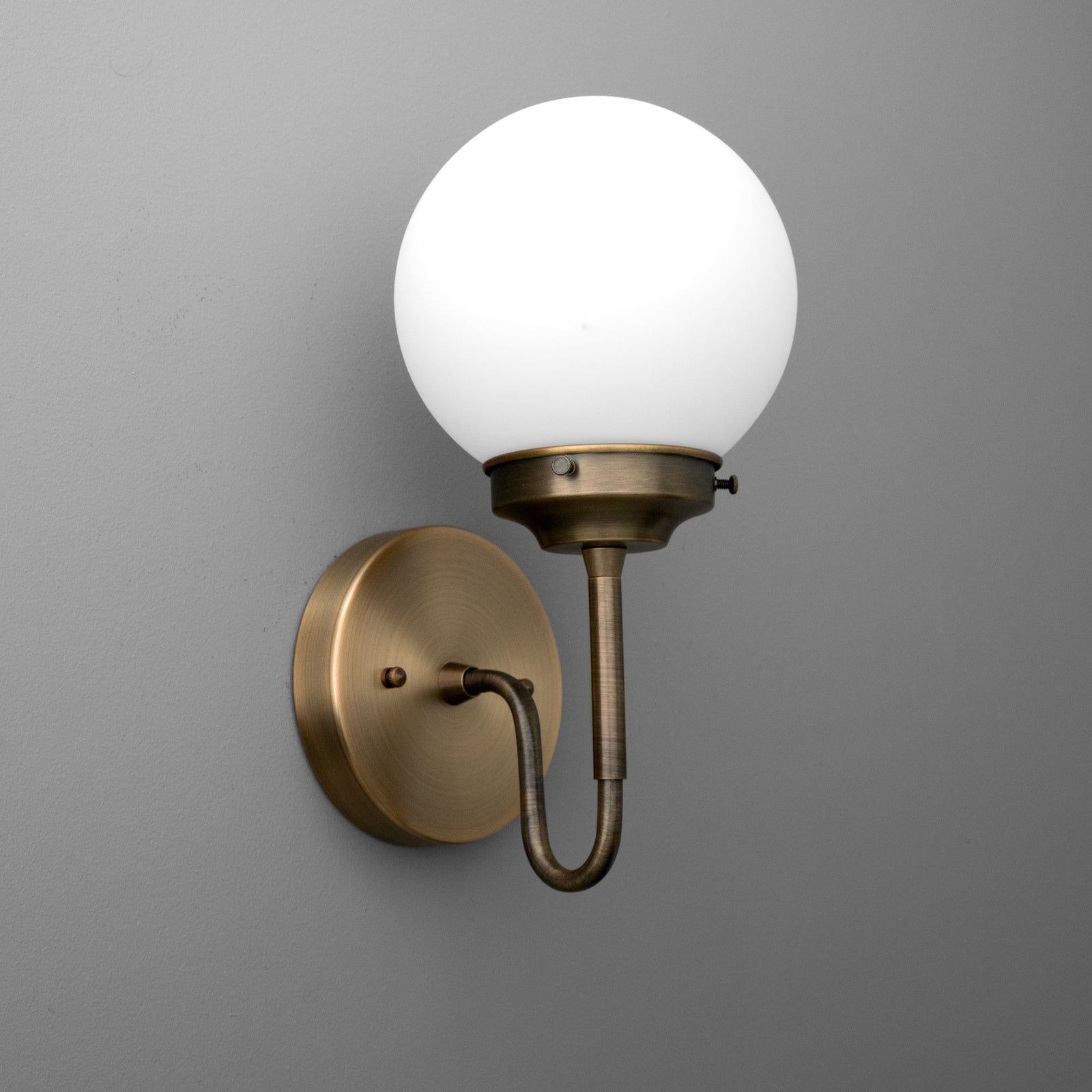 Wall-mounted sconce with a round white glass globe and antique brass finish curved arm and base. - SCONCE MODEL NO. 3690