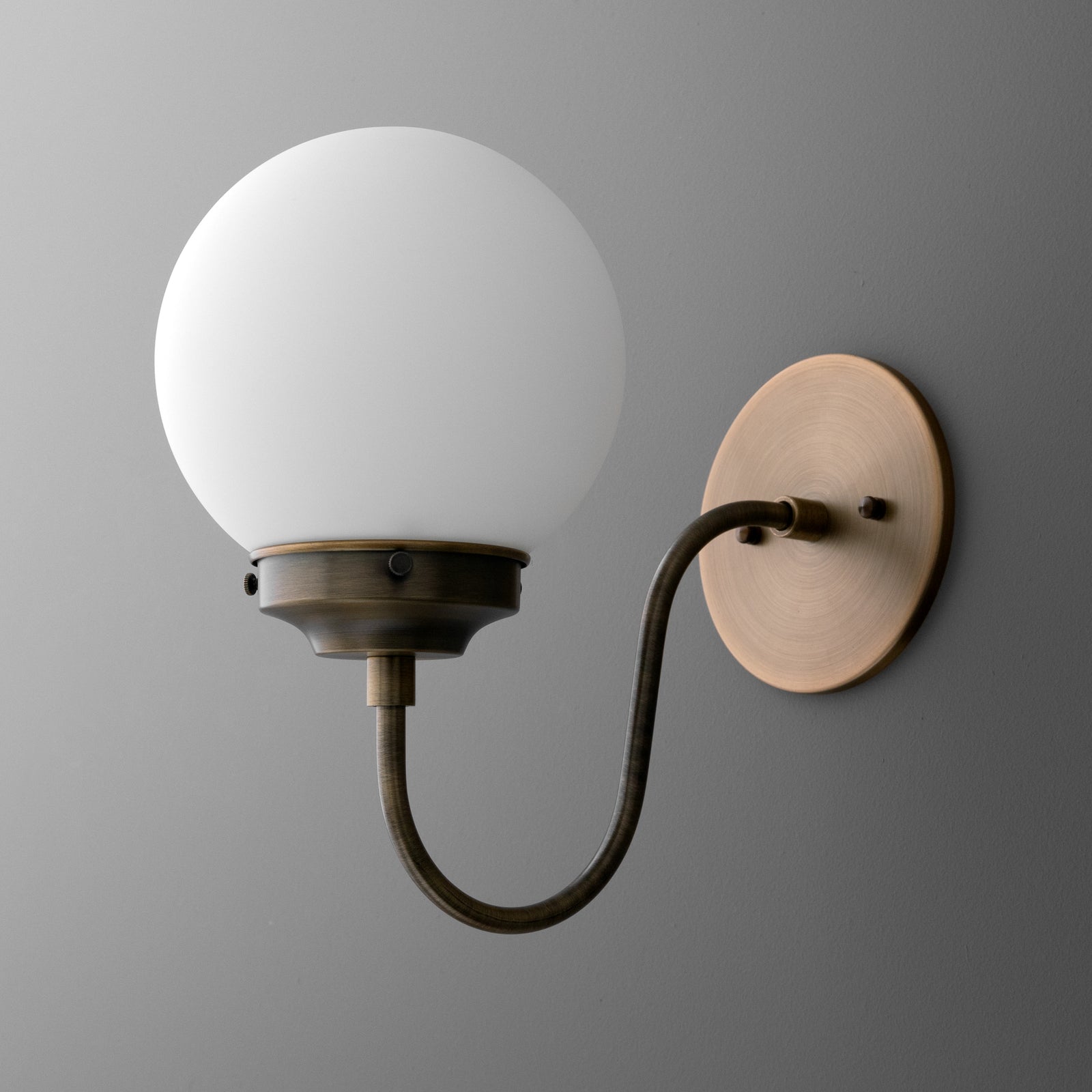 Wall-mounted sconce with round frosted glass globe and curved antique brass arm on a circular base. - SCONCE MODEL NO. 1886