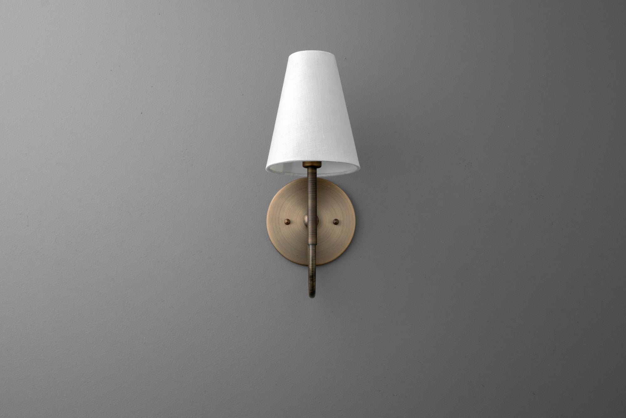 Wall sconce with antique brass finish and white tapered fabric shade mounted on gray wall. - SCONCE MODEL NO. 4594