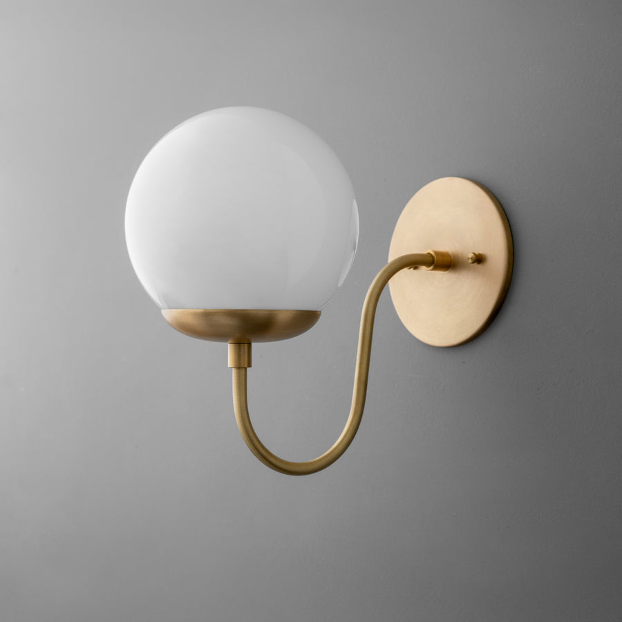 Wall-mounted sconce with a raw brass curved arm and a round white glass globe shade on a circular backplate. - SCONCE MODEL NO. 3849