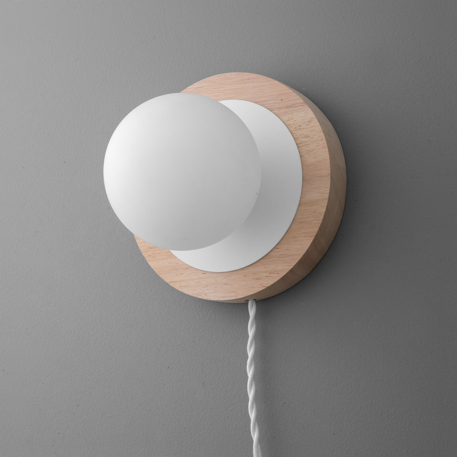 Minimalist wall sconce with white globe shade and natural wood round base on gray wall. - SCONCE MODEL NO. 6154