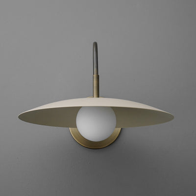 Antique brass wall sconce with a cream flat disc shade and white globe bulb against gray wall. - SCONCE MODEL NO. 9171