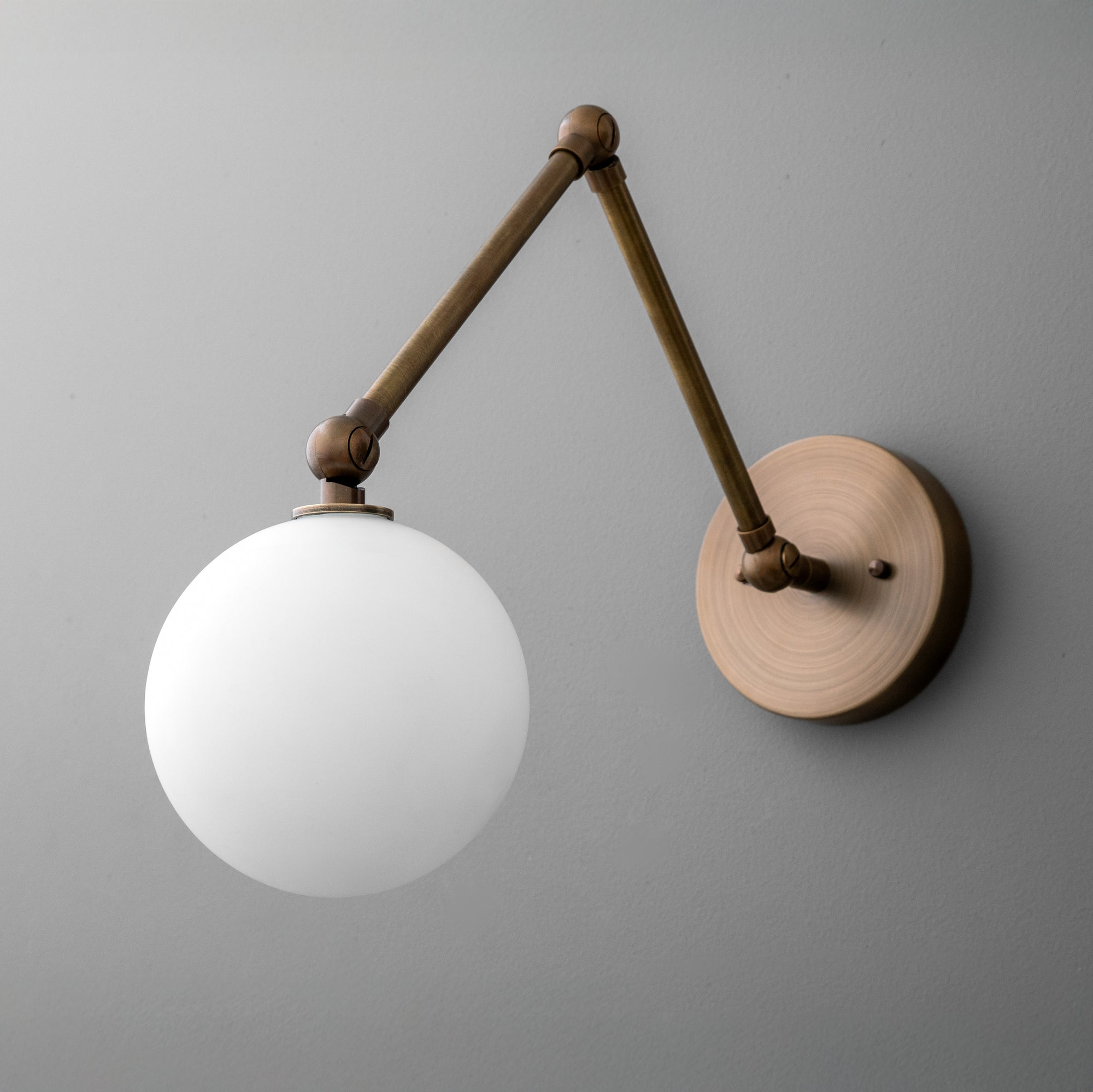 Wall sconce with adjustable antique brass arm and frosted white globe shade mounted on round brass base. - SCONCE MODEL NO. 5202