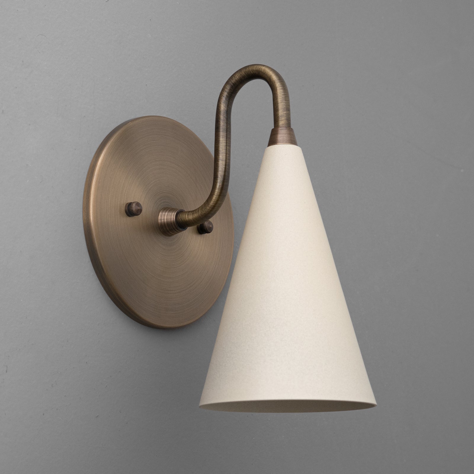 Antique brass sconce with a smooth cream tapered shade against gray wall. - Sconce Model No. 2900