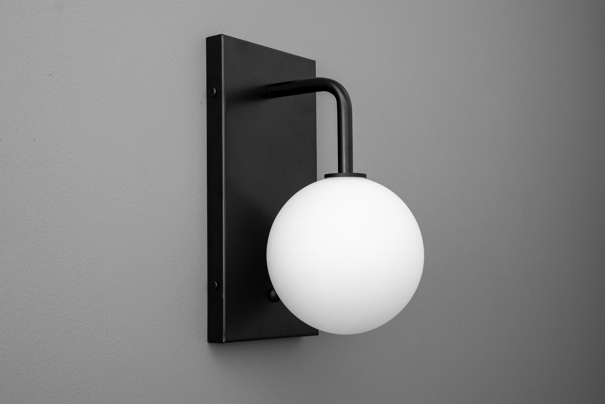 Matte black wall sconce with curved arm and frosted white glass globe shade. - SCONCE MODEL NO. 9002