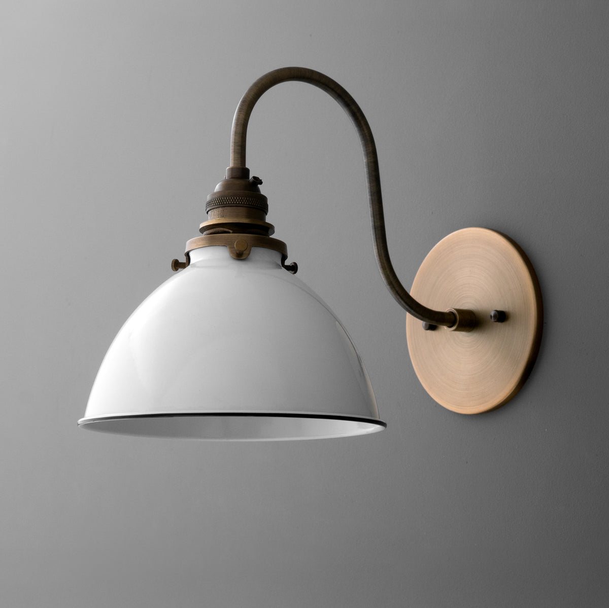 Single-light sconce in Antique Brass with a long gooseneck arm and exposed socket holding a metal dome shade, on a round wall plate. - SCONCE MODEL NO. 4055