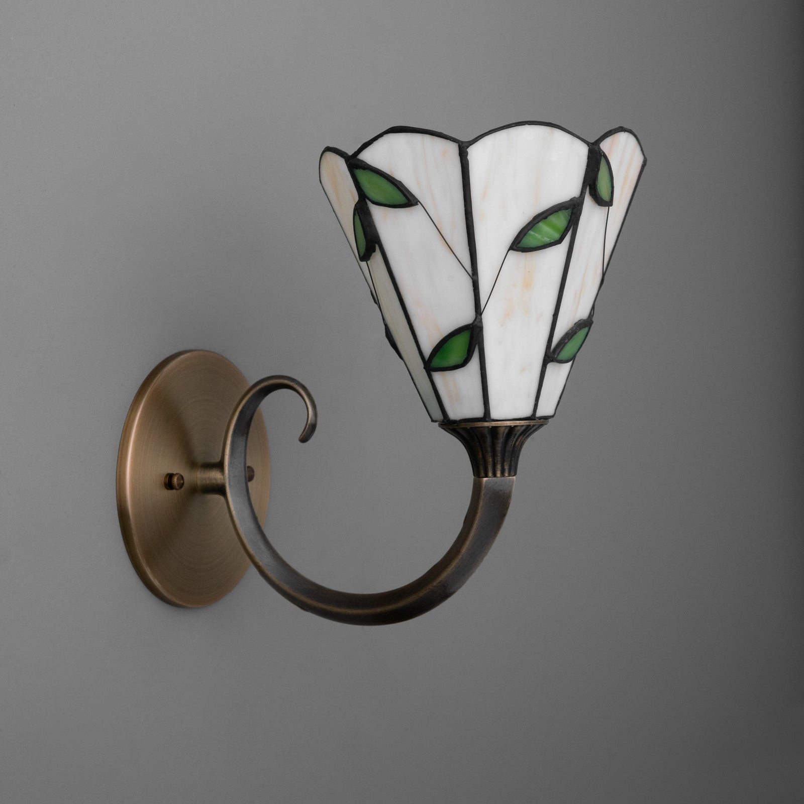 Wall-mounted bronze sconce with curved arm and white stained glass shade featuring green leaf accents. - SCONCE MODEL NO. 1056