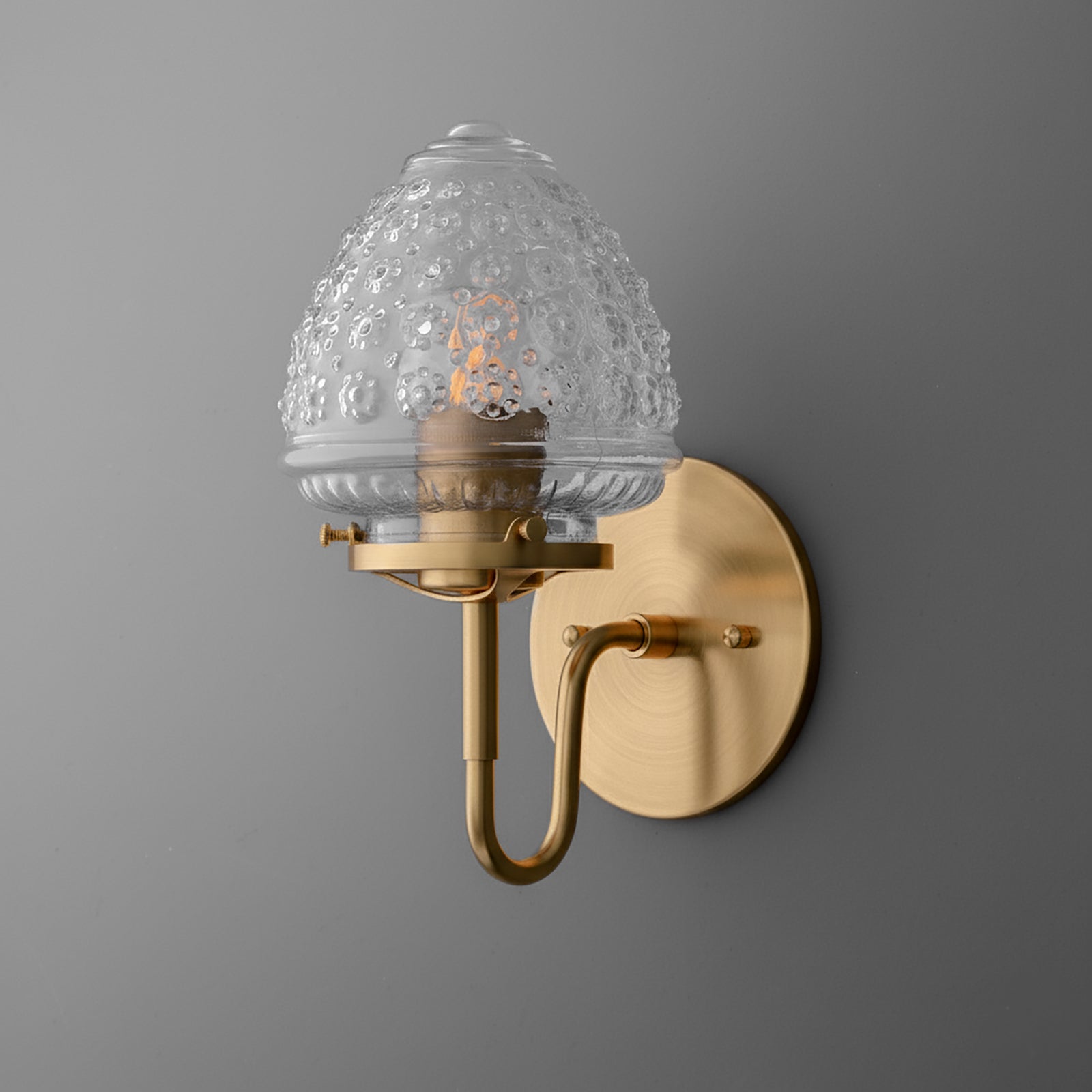 Brushed brass single-bulb wall sconce with textured clear glass shade and curved arm. - SCONCE MODEL NO. 1037