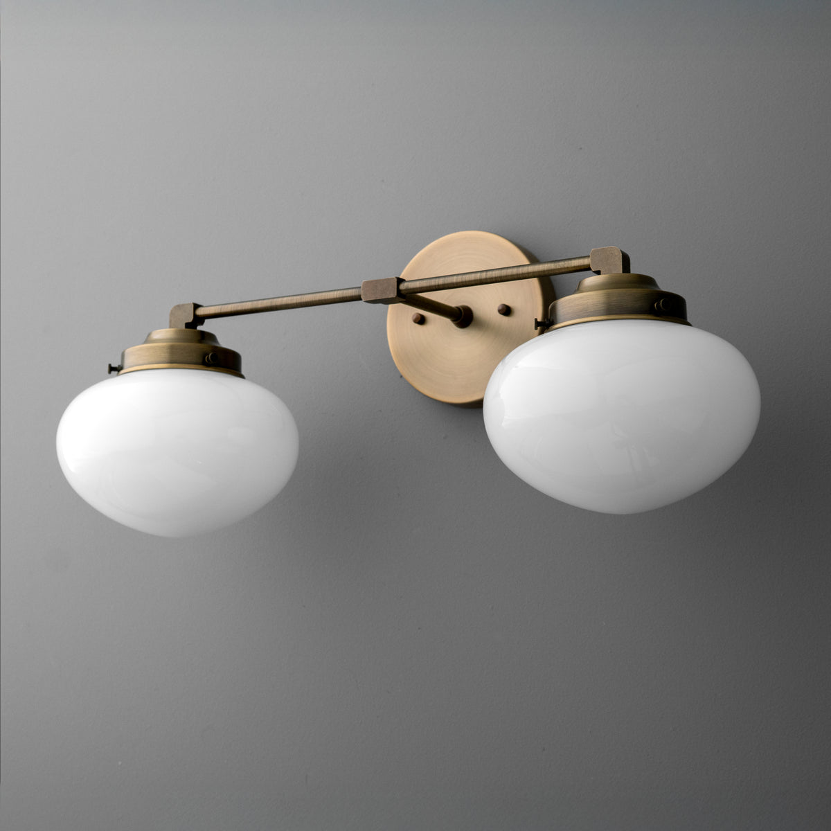 Two-bulb vanity light with frosted white glass shades and brushed brass metal frame mounted on gray wall. - VANITY LIGHT MODEL NO. 1167