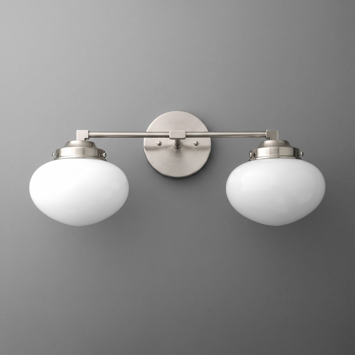 Brushed nickel vanity light with two round white frosted glass shades mounted on a straight horizontal bar. - VANITY LIGHT MODEL NO. 1167