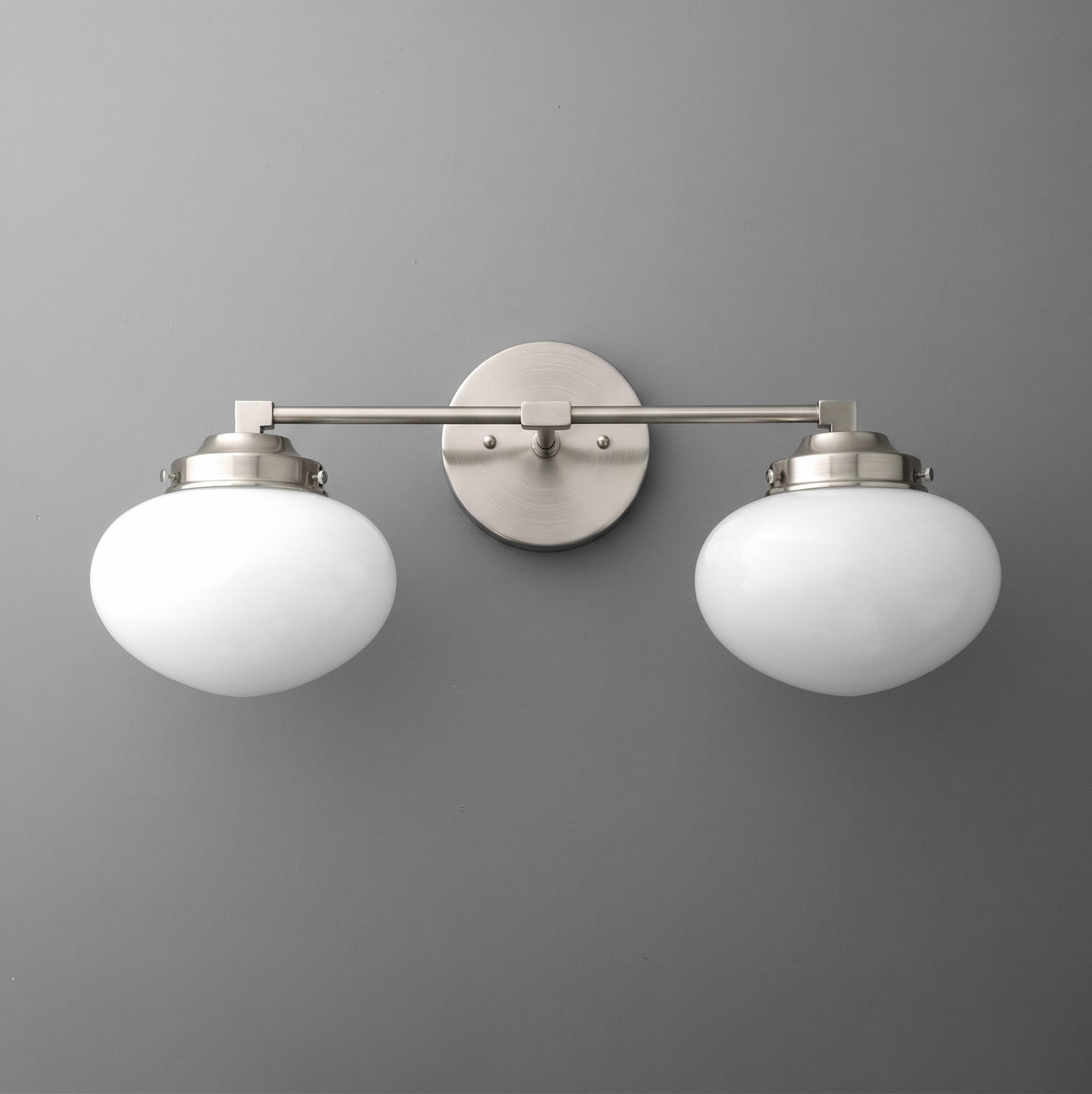 Brushed nickel vanity light with two round white frosted glass shades mounted on a straight horizontal bar. - VANITY LIGHT MODEL NO. 1167