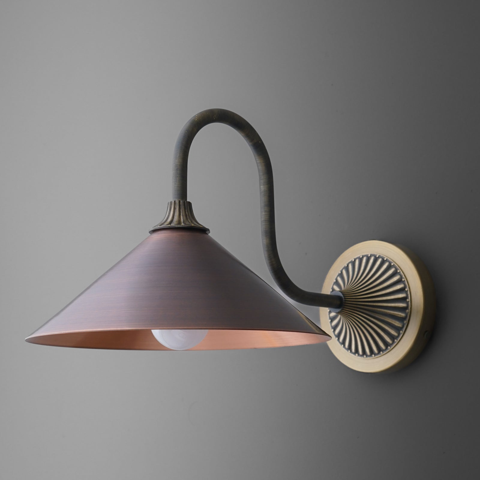 Wall-mounted sconce with matte black curved arm, bronze circular backplate, and wide conical bronze shade. - SCONCE MODEL NO. 1055