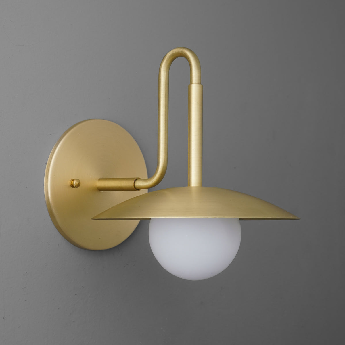 Matte gold metal wall sconce with round backplate and flat disk shade above frosted glass globe bulb. - SCONCE MODEL NO. 1013