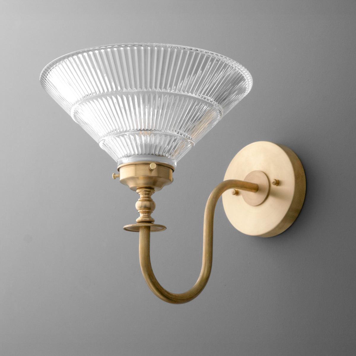 Wall sconce with ribbed clear glass shade and brushed brass curved arm and round wall mount. - SCONCE MODEL NO. 8036