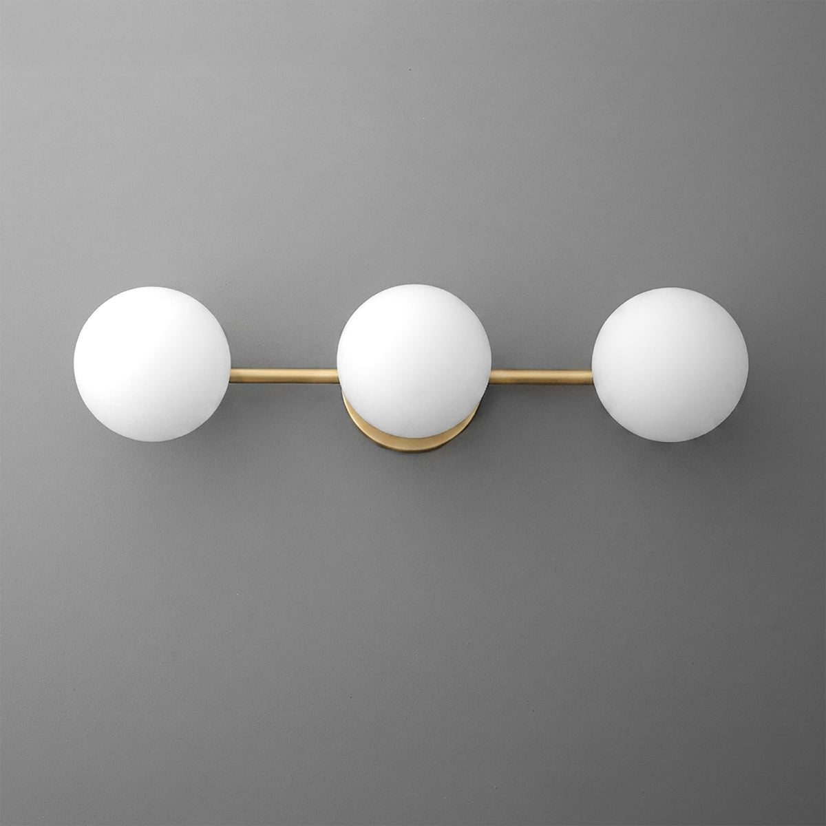 Three-globe vanity light with frosted white glass shades and brushed brass horizontal bar mount on gray wall. - VANITY LIGHT MODEL NO. 9250