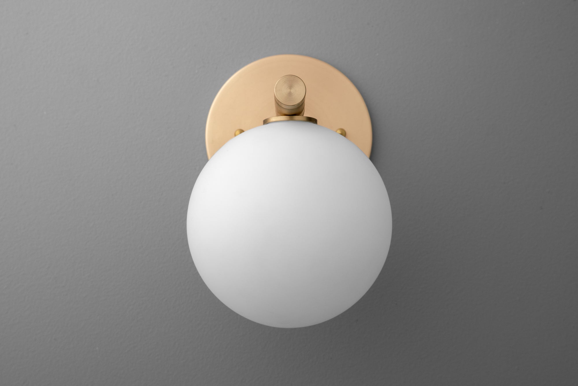 Round white glass globe wall sconce with raw brass circular base on gray background. - SCONCE MODEL NO. 0904