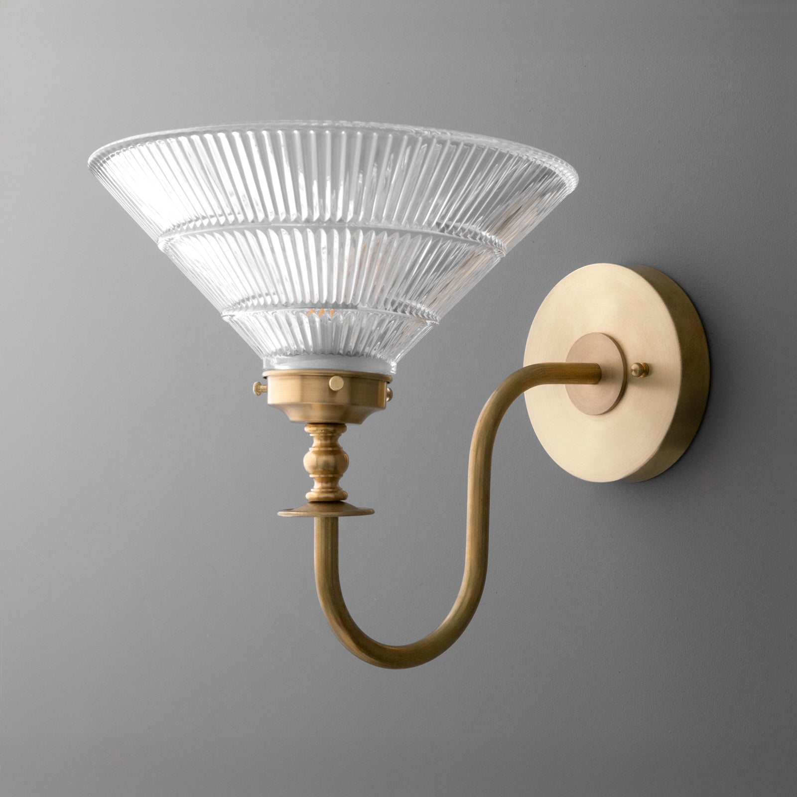 Wall sconce with a curved brass arm and ribbed glass conical shade mounted on a round brass base. - SCONCE MODEL NO. 8036