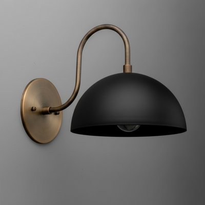 Matte black dome sconce with antique brass curved arm and round wall mount against gray wall. - SCONCE MODEL NO. 9092