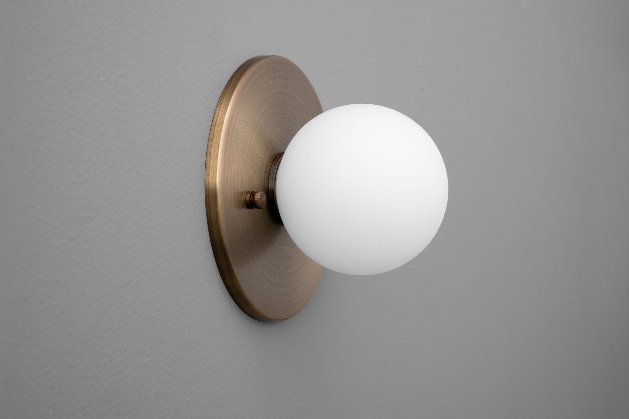 Antique brass sconce with 5-inch white frosted glass globe on round backplate. - Sconce Model No. 5206