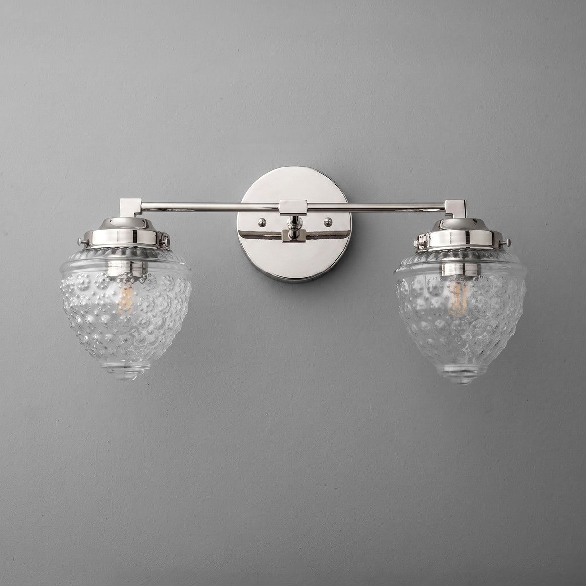 Two-bulb vanity light with brushed nickel finish and textured clear glass shades mounted on round wall plate. - VANITY LIGHT MODEL NO. 1155