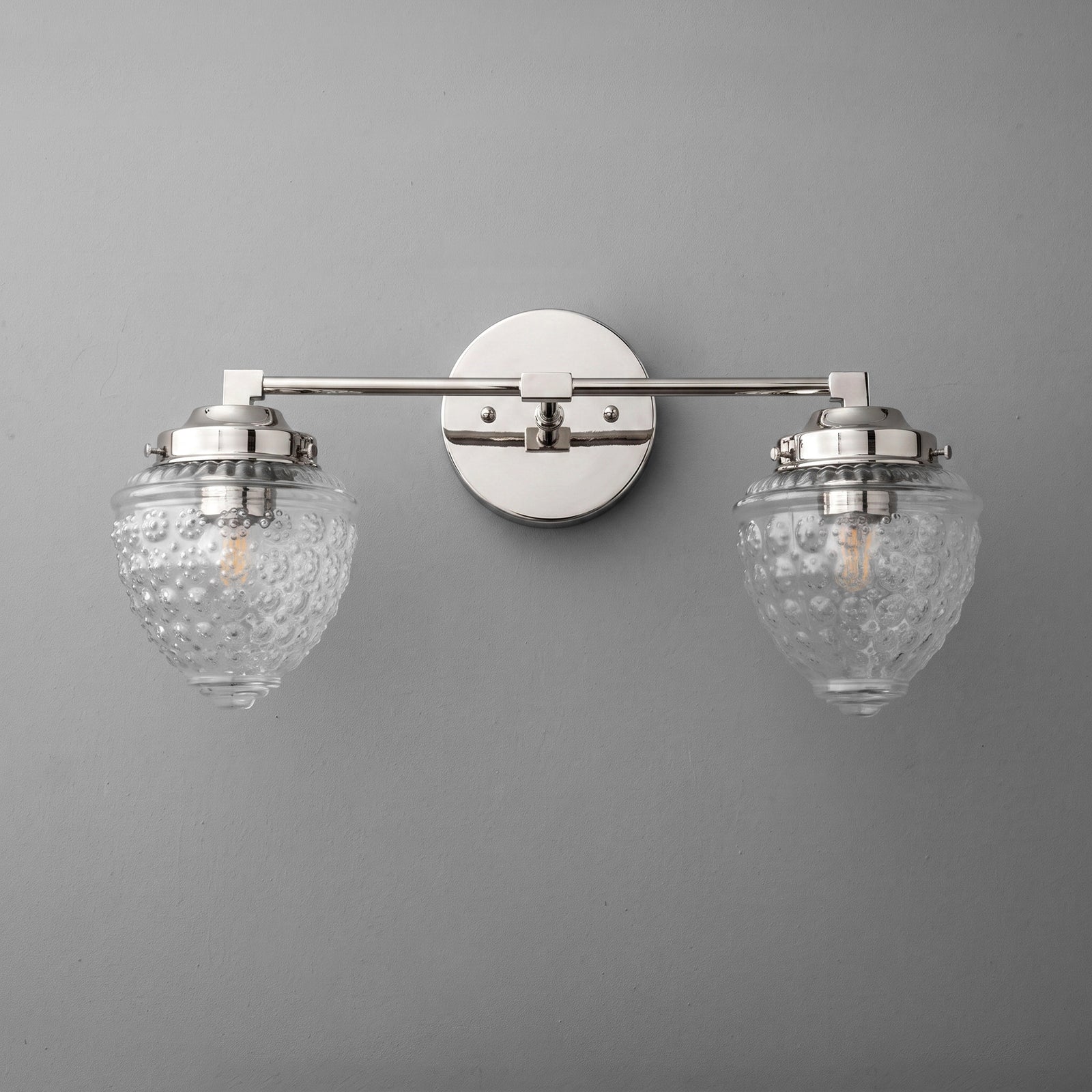 Two-bulb vanity light with brushed nickel finish and textured clear glass shades mounted on round wall plate. - VANITY LIGHT MODEL NO. 1155
