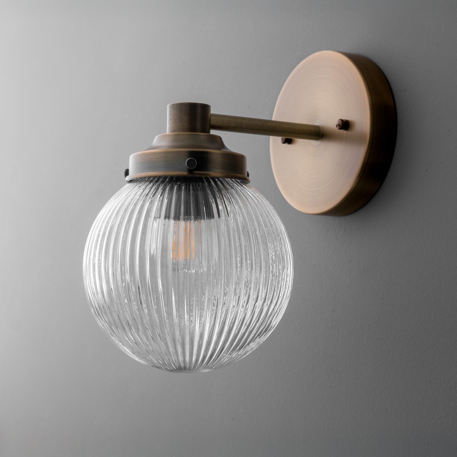 Wall sconce with ribbed clear glass globe and matte brass finish mounting plate and arm. - SCONCE MODEL NO. 7273