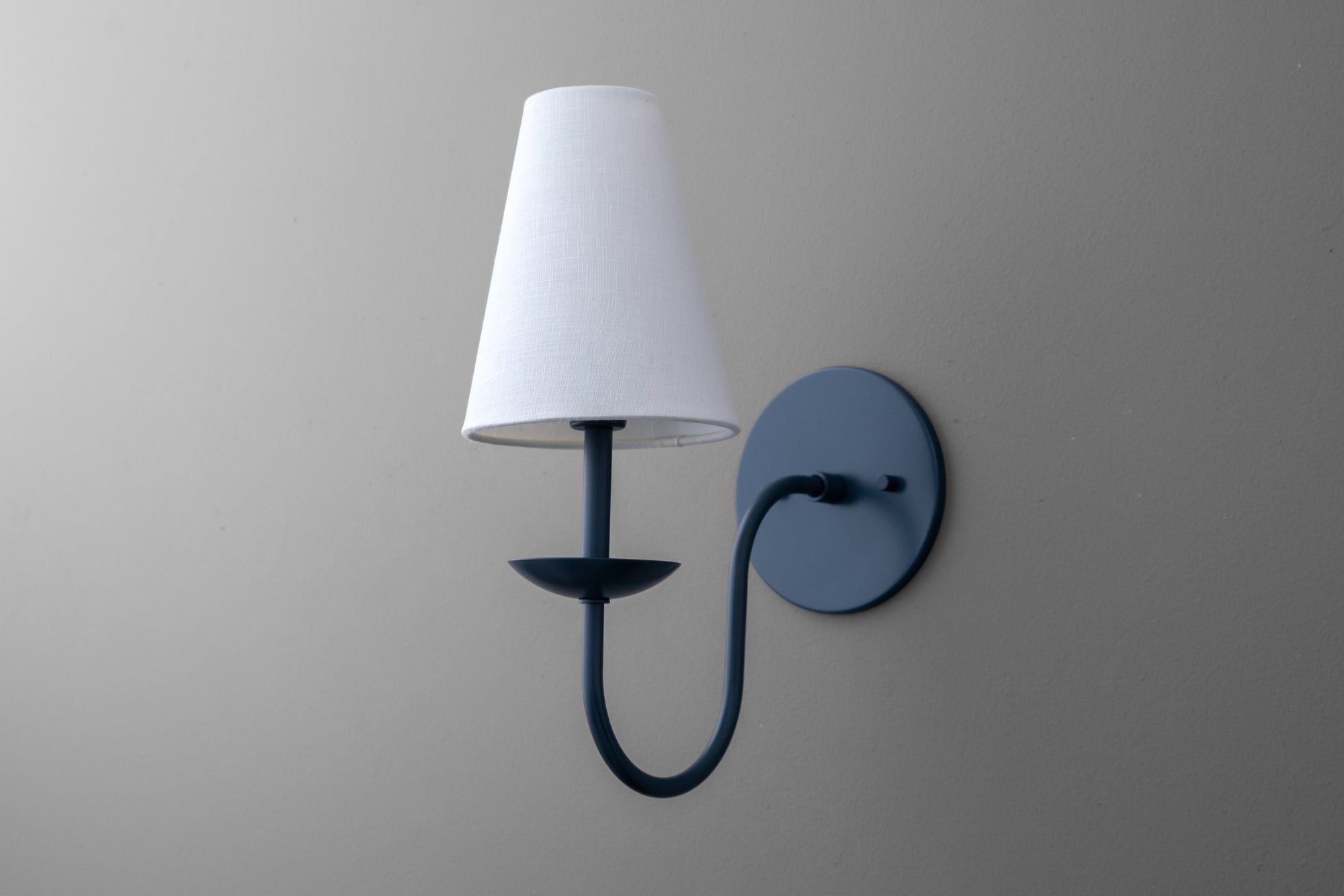 Wall-mounted black metal sconce with curved arm and white tapered fabric shade. - SCONCE MODEL NO. 7085