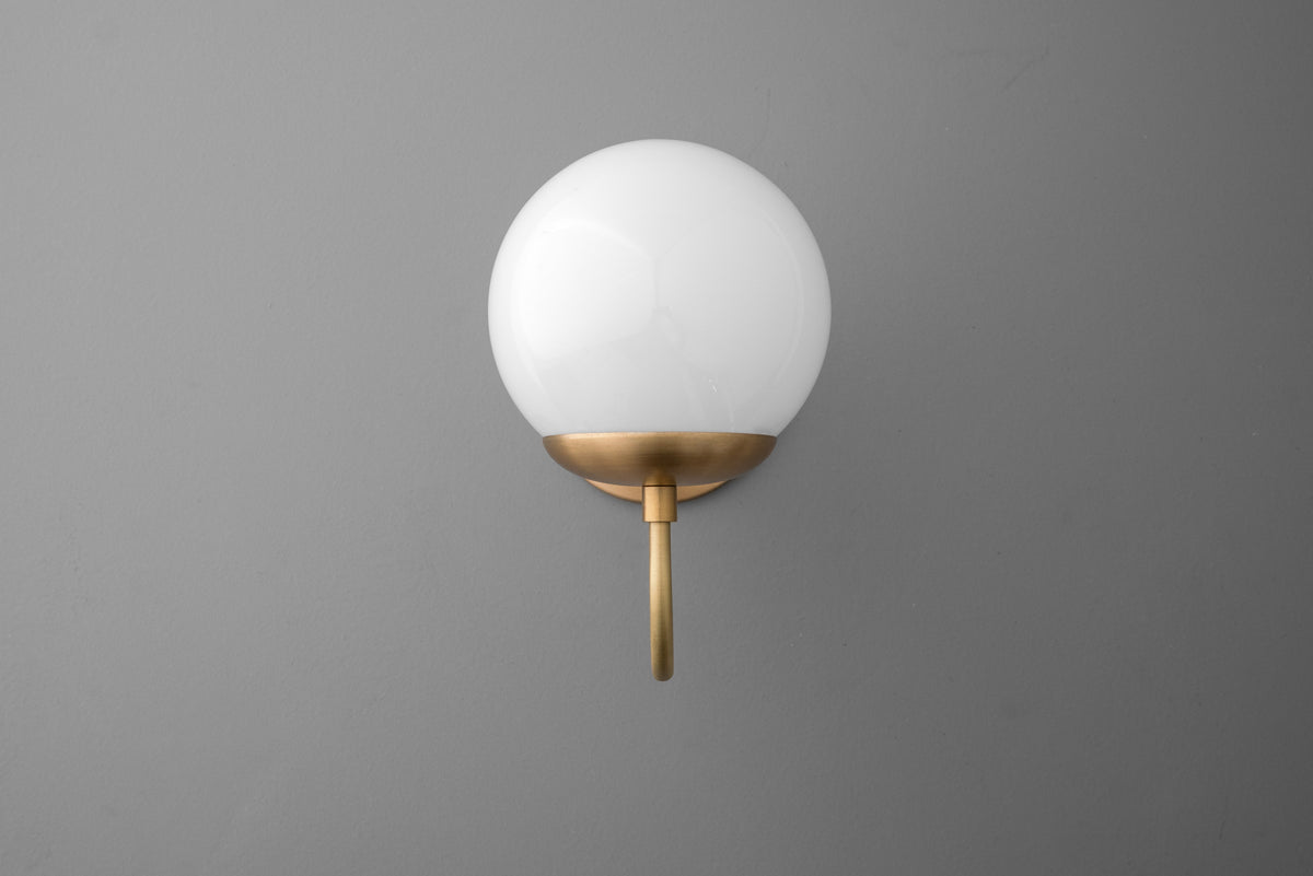 Wall sconce with a round white glass globe and raw brass mount on matte gray wall. - SCONCE MODEL NO. 3849