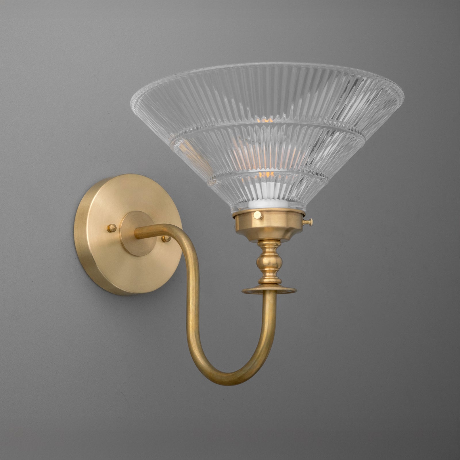Wall sconce with curved brass arm and flared ribbed glass shade with visible light bulb. - SCONCE MODEL NO. 8036