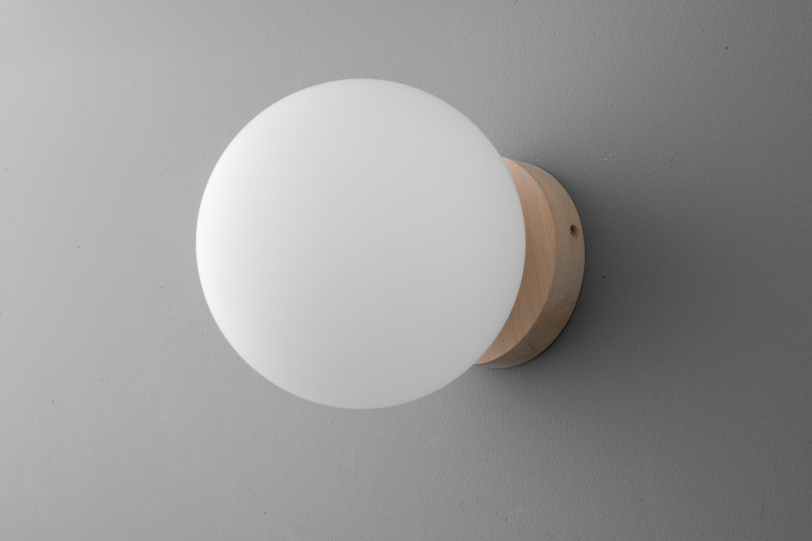 Minimalist round white glass globe sconce with light wood base mounted on gray wall. - SCONCE MODEL NO. 4943