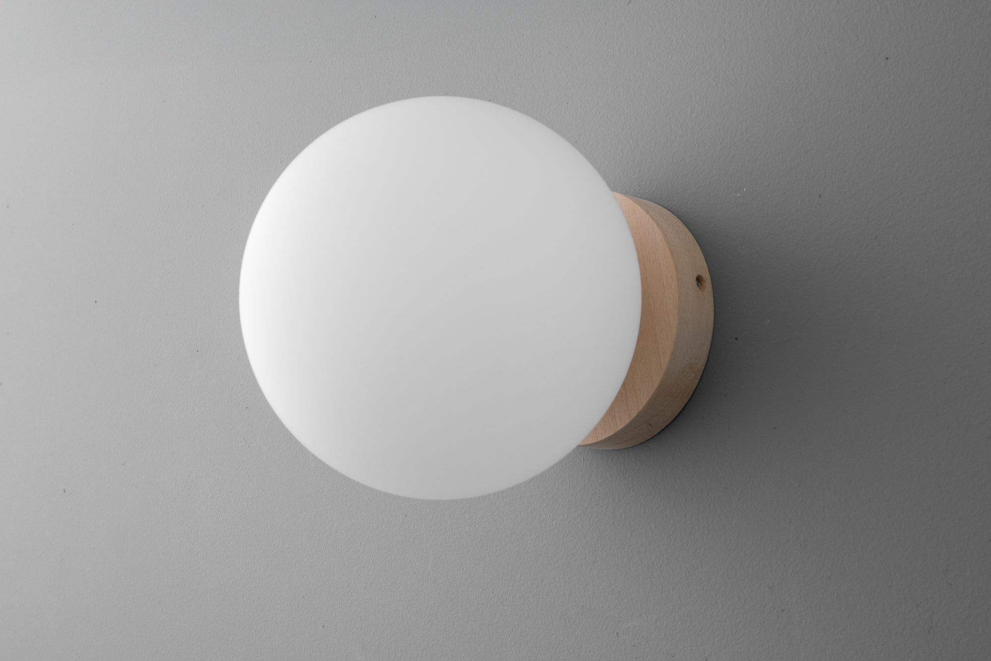 Minimalist round white glass globe sconce with light wood base mounted on gray wall. - SCONCE MODEL NO. 4943