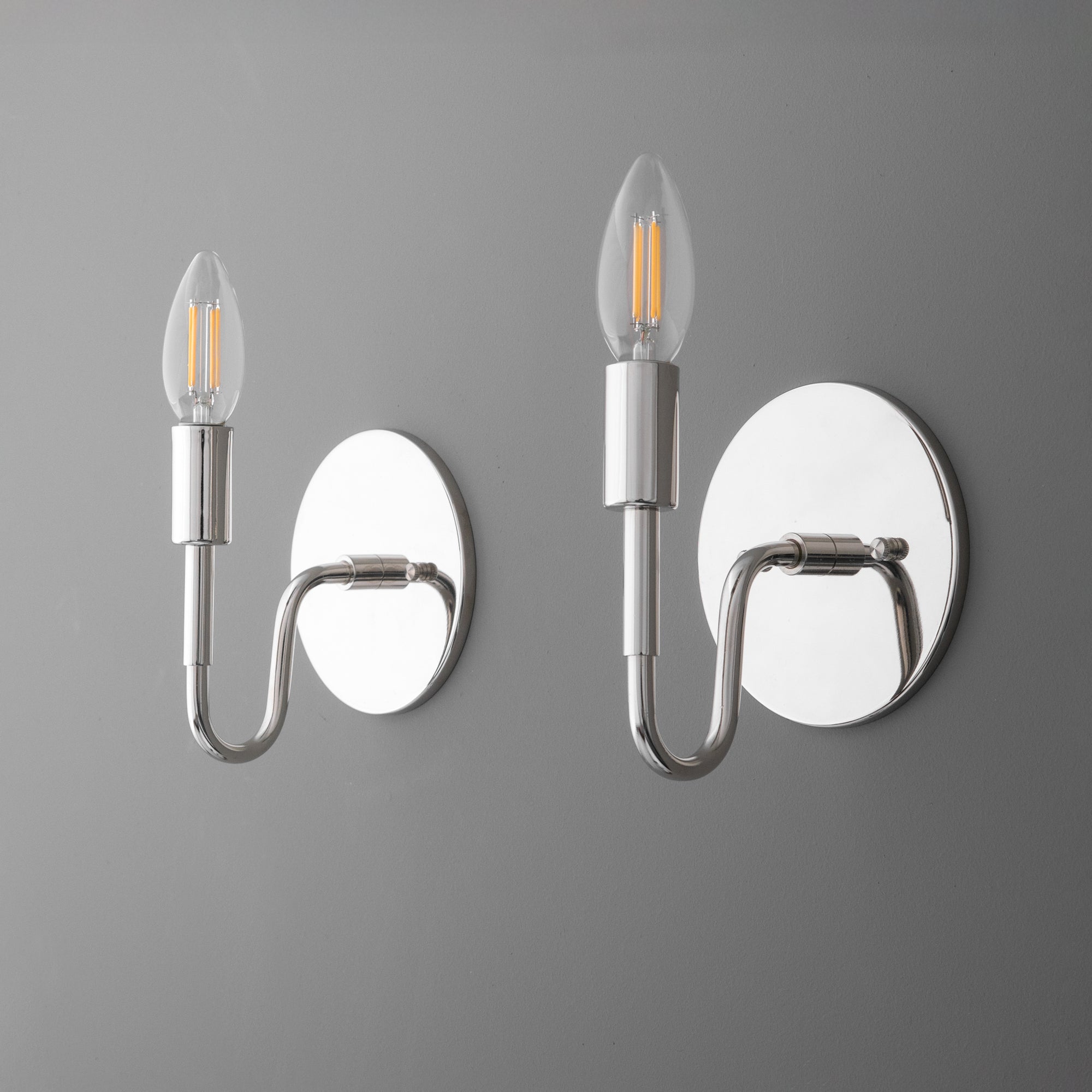 Pair of modern silver metal wall sconces with exposed elongated filament bulbs and round backplates. - SCONCE MODEL NO. 1100
