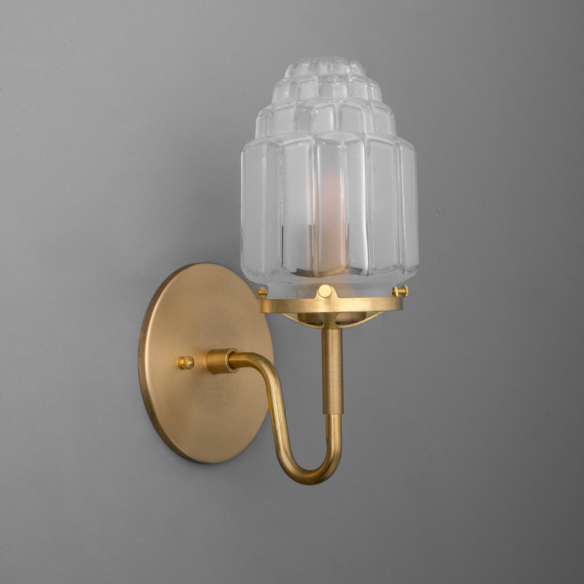 Brushed brass wall sconce with curved arm and tiered ribbed clear glass shade covering one bulb. - SCONCE MODEL NO. 1035