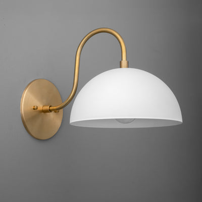 Raw brass wall sconce with curved arm and white dome-shaped shade on gray background. - SCONCE MODEL NO. 9092
